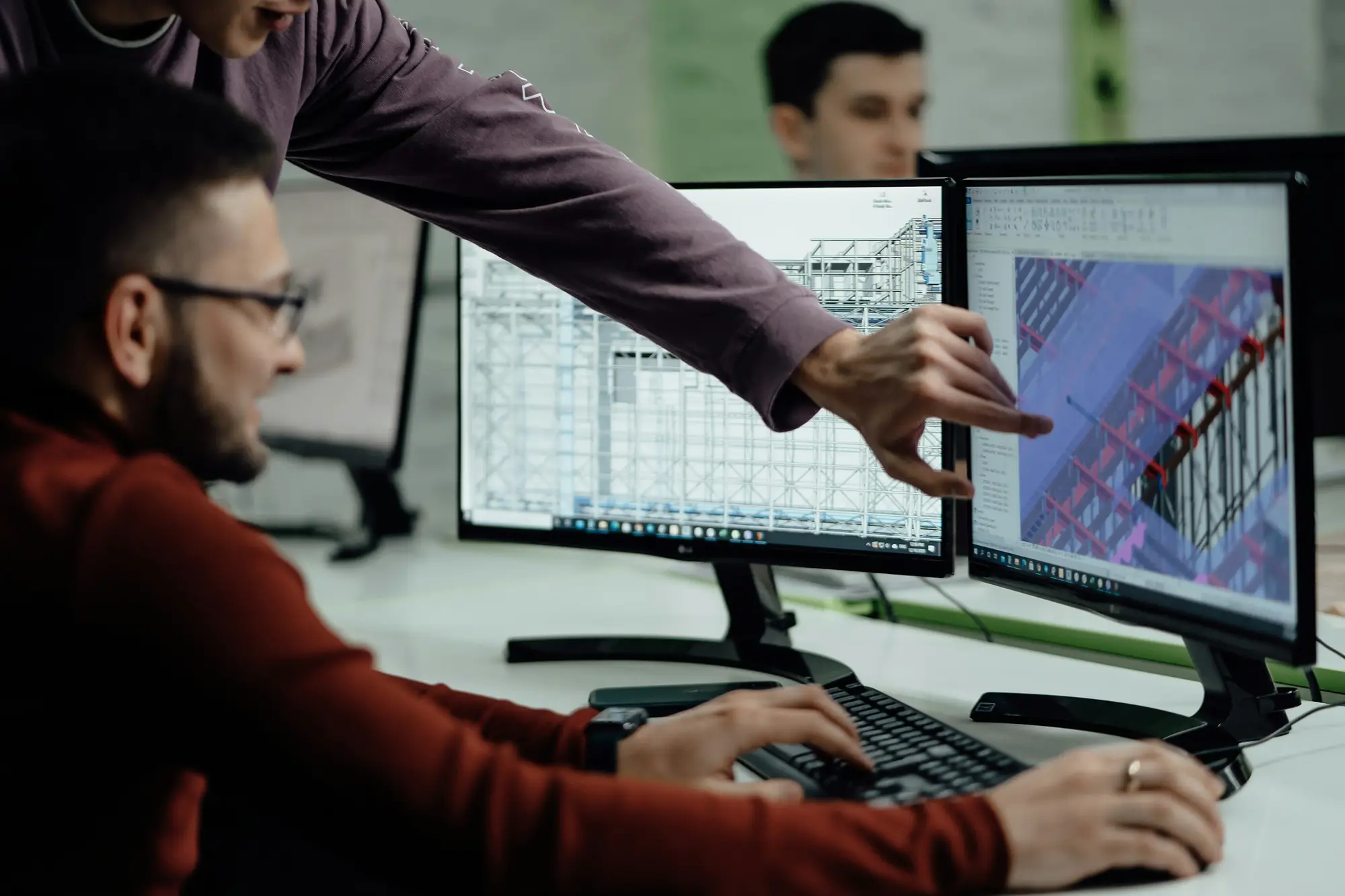 Engineers reviewing a 3D structural steel model on two desktop monitors in a bright office